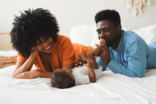 Free A joyful family scene with parents bonding with their baby in a cozy indoor setting. Stock Photo