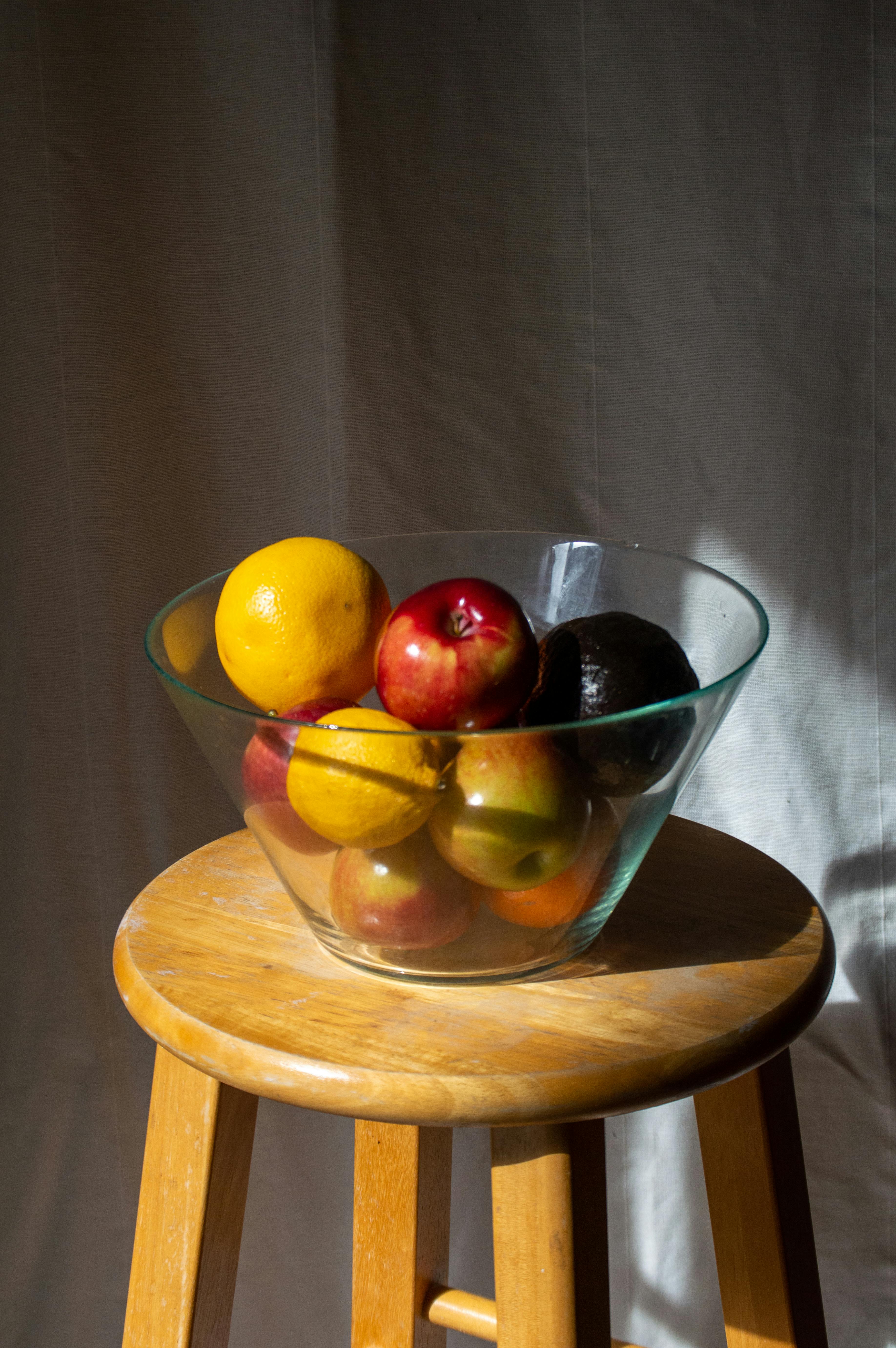 A vibrant fruit bowl with apples, lemons, and avocado on a stool.