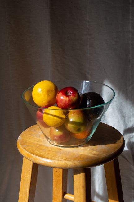 A vibrant fruit bowl with apples, lemons, and avocado on a stool.