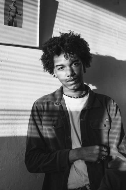 Stylish young man with afro hair and beaded necklace in a black-and-white portrait.