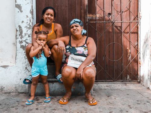 Free Mother and daughter smiling as they pose with a senior woman outside a rustic doorway. Stock Photo
