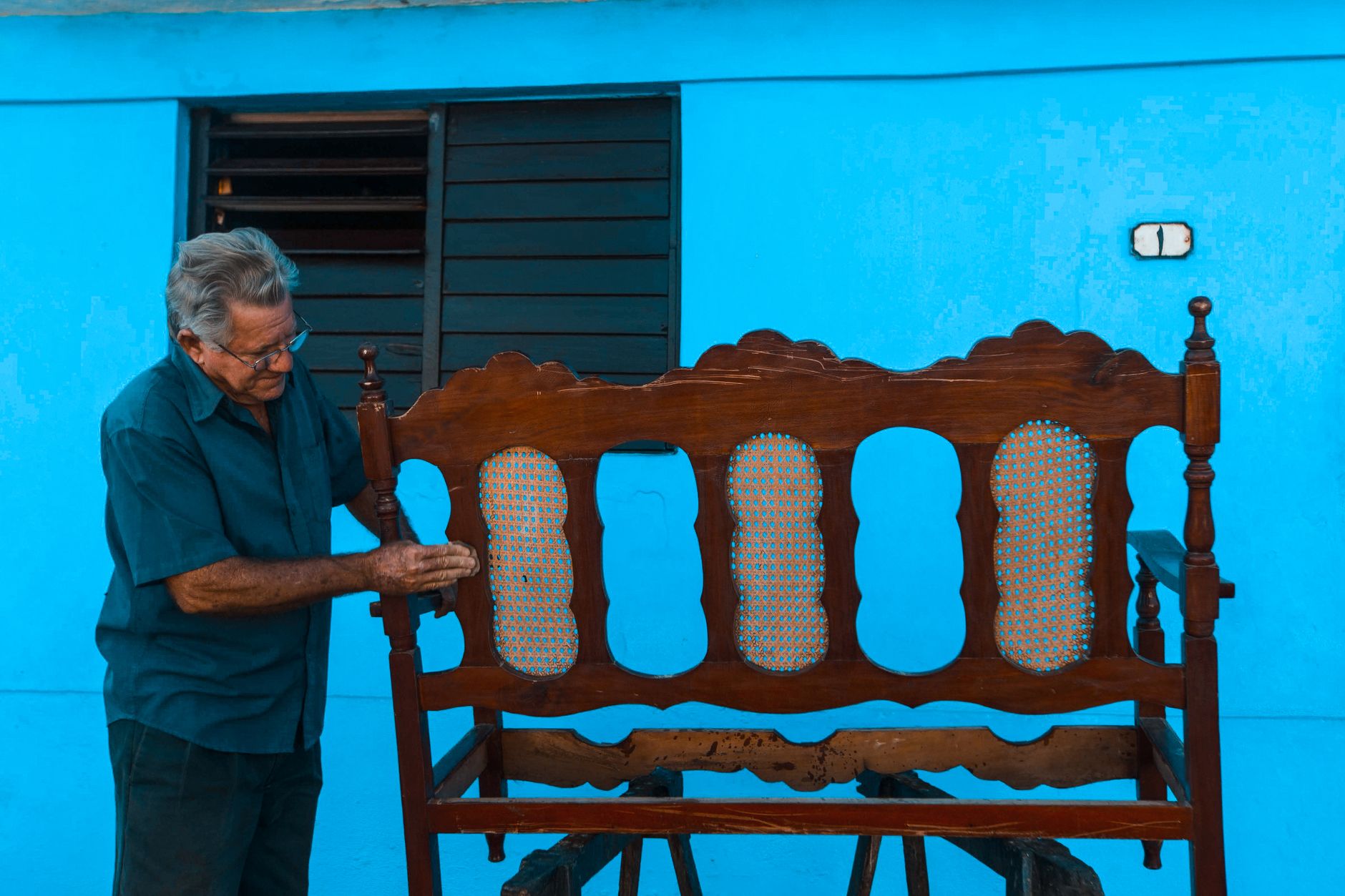 DIY Simple Bench Using Home Depot Lumber An elderly man restoring a vintage wooden bench against a bright blue wall