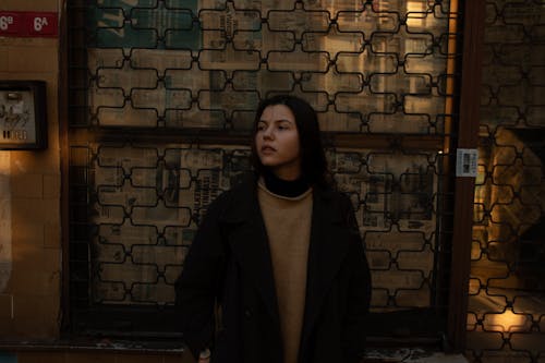 Free Woman in Black Coat Standing Beside Brick Wall Stock Photo