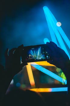 Hands holding smartphone recording neon lights at a night event.