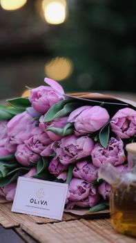 Elegant bouquet of pink tulips next to a business card and honey jar, captured outdoors.