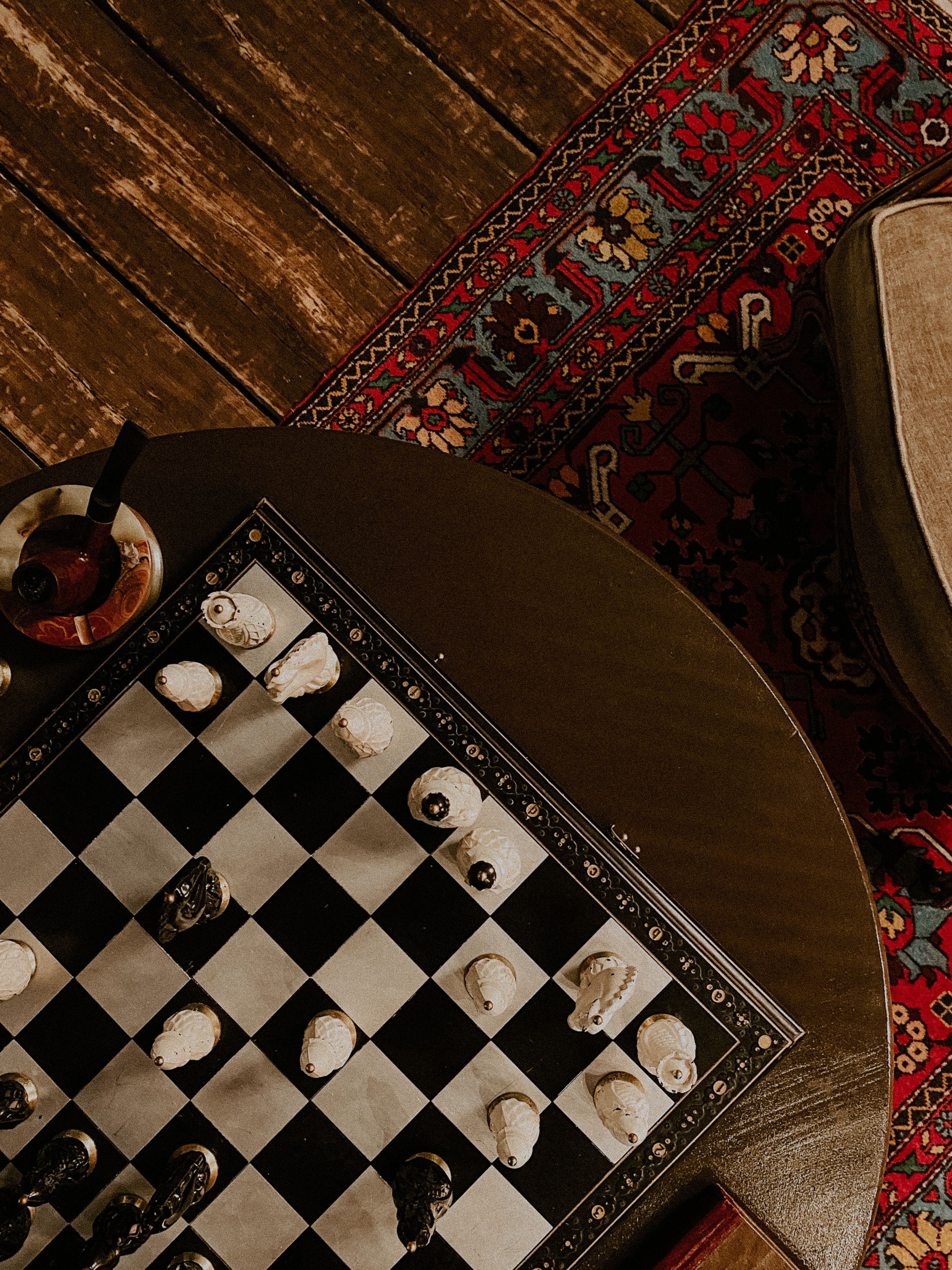 A vintage chessboard on a Persian rug, with a pipe on the side. Cozy and classic setting.