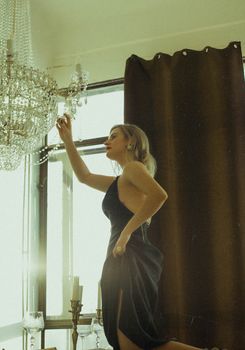 A woman in a black dress adjusts a chandelier indoors, capturing an elegant moment.