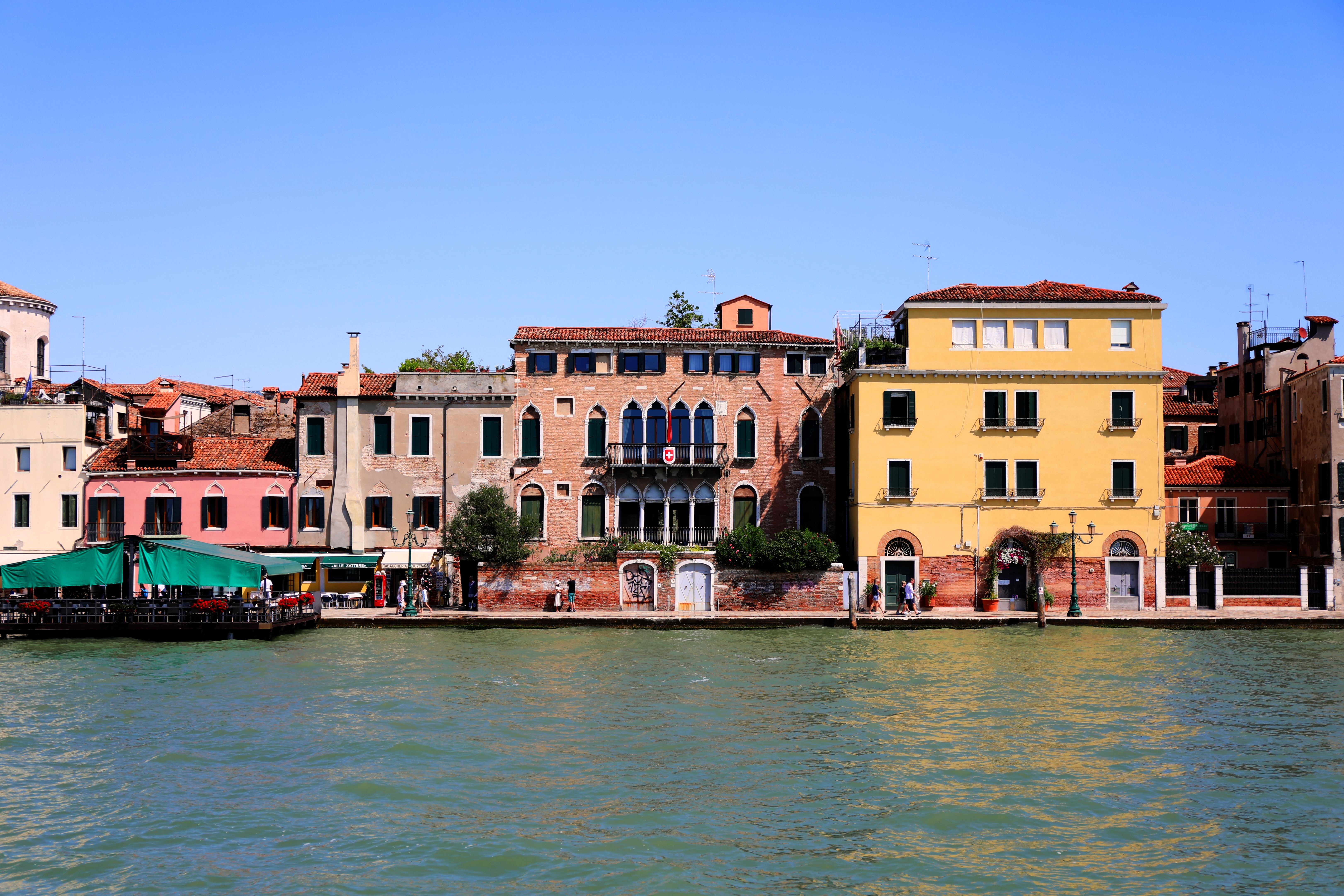 Colorful Venetian buildings along a serene canal under a clear blue sky, showcasing classic architecture.