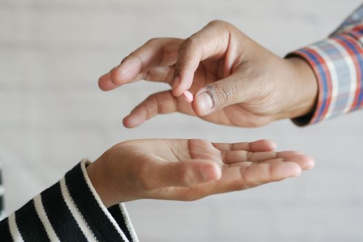 Close-up of hands exchanging a single pill, symbolizing medication sharing.
