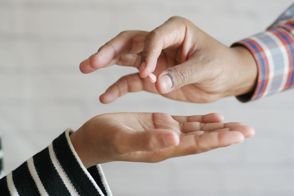 Close-up of hands exchanging a single pill, symbolizing medication sharing.