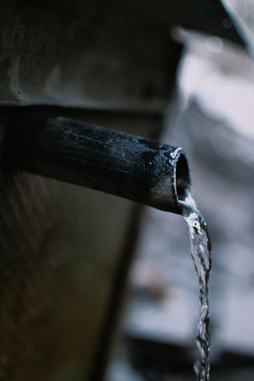Free Flowing water from metal pipe showcasing motion and fluidity in an industrial setting. Stock Photo