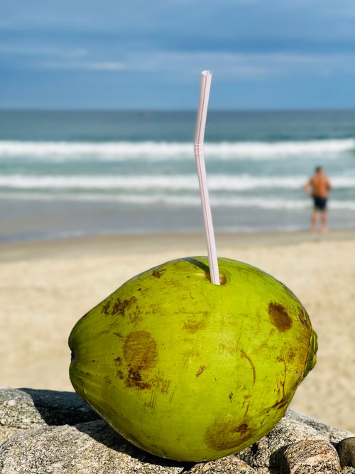 Free Close-up of a coconut with straw on Ubatuba beach, Brazil, with ocean and person in the background. Stock Photo