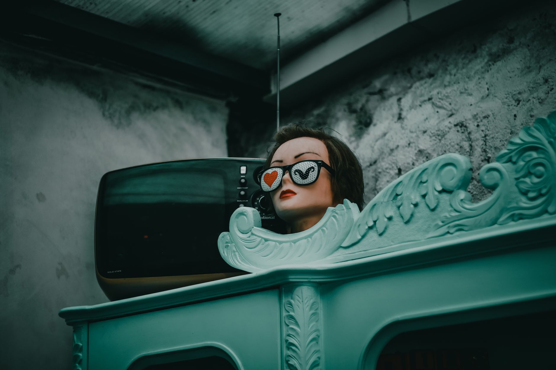 A mannequin with heart-shaped sunglasses beside a retro TV in a vintage setting, exuding nostalgia.