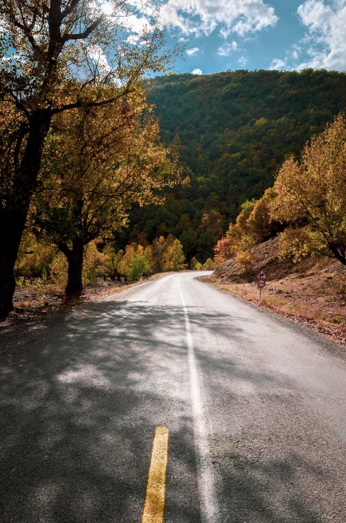 Free Empty road through autumn countryside with colorful trees and hills in the background. Stock Photo
