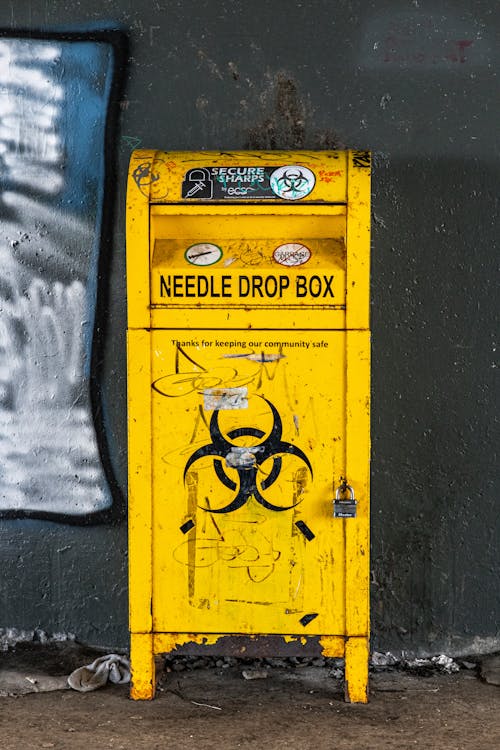 A Yellow Steel Needle Drop Box Beside Black Wall