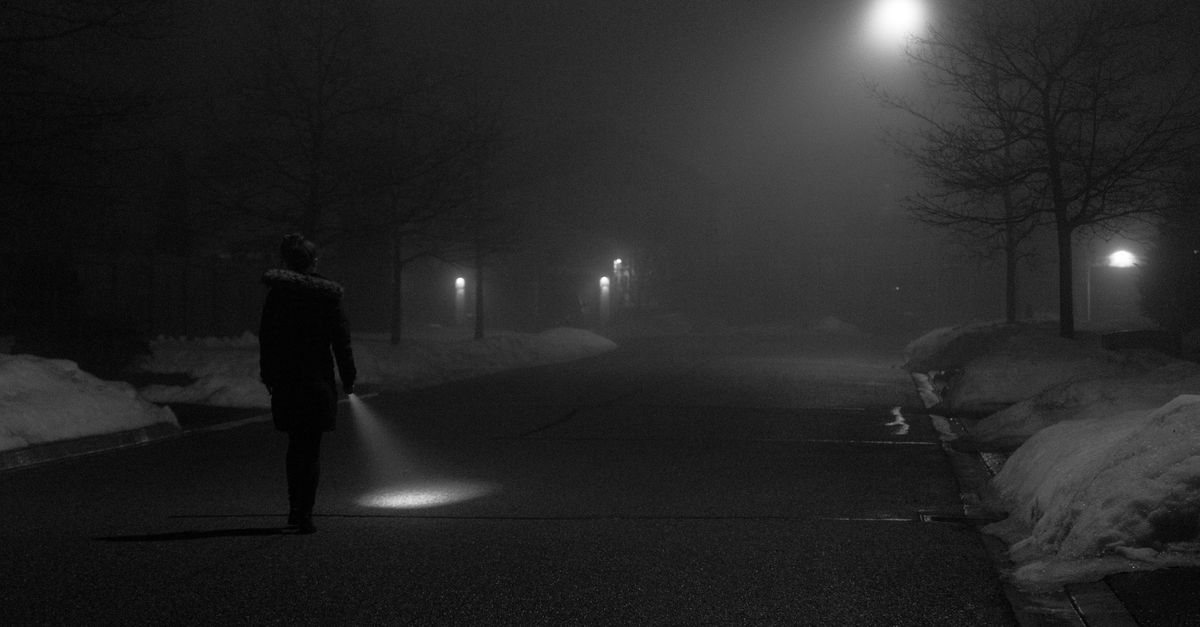 person walking on a foggy path with a small flashlight illuminating just a few feet ahead