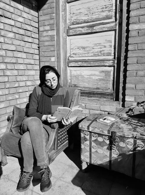 A Woman Sitting on a Chair while Reading a Book