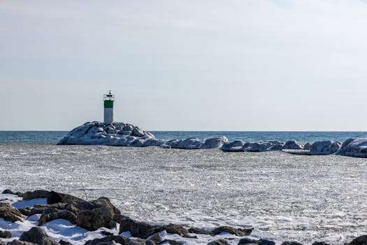 A lighthouse stands on an ice-covered shoreline against a clear winter sky.