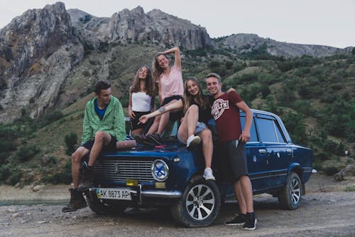A Group of Friends Sitting on the Car Parked Near the Mountain