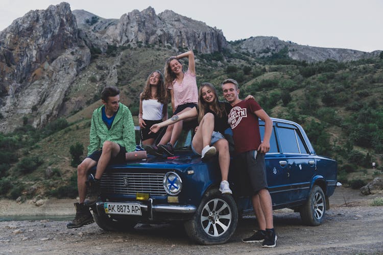 A Group Of Friends Sitting On The Car Parked Near The Mountain