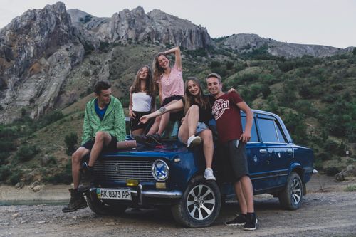 Free Group of friends sitting on a classic car in the mountains, enjoying a road trip adventure. Stock Photo