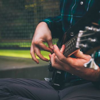 Musician strumming a bass guitar in an outdoor setting, capturing the essence of music.