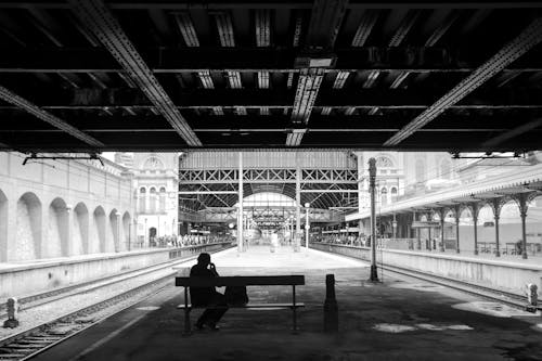 Free Monochrome Shot of a Person Sitting on a Bench in a Train Station Stock Photo