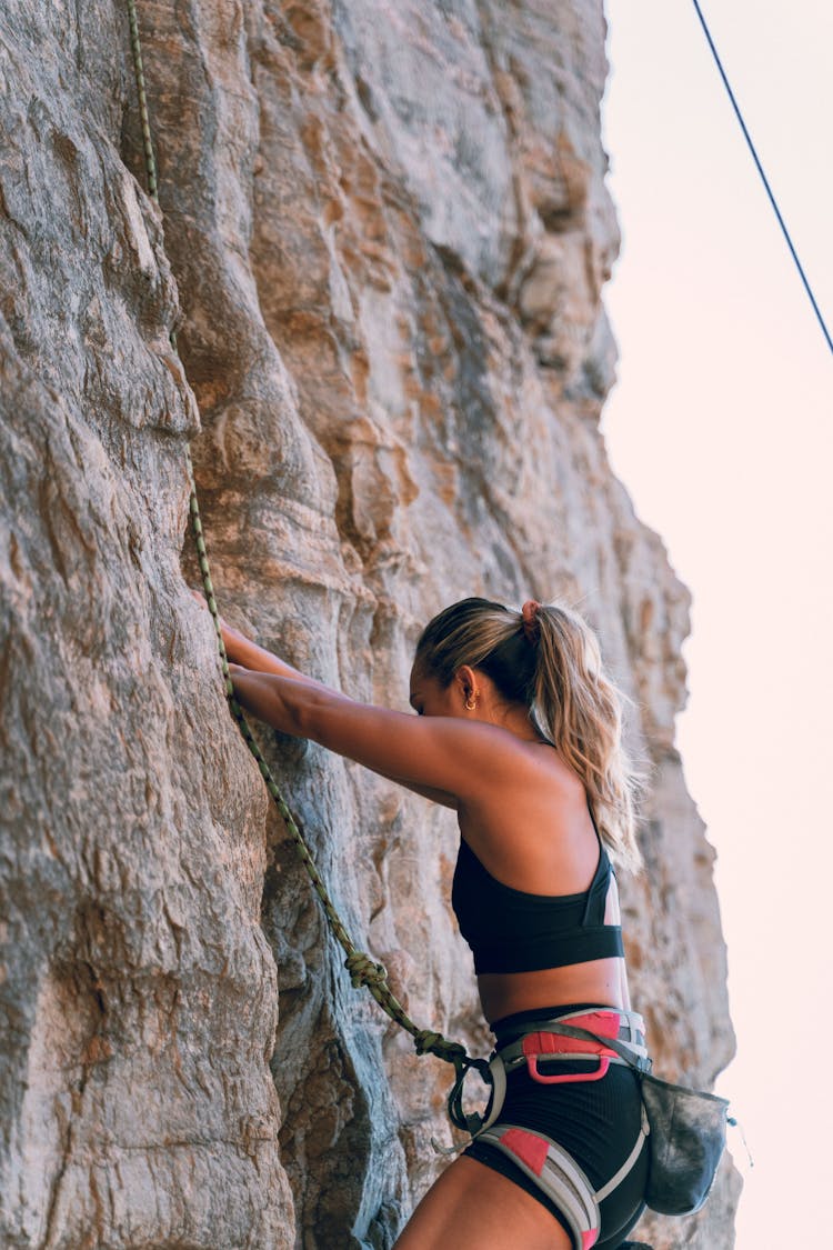 Woman In Black Sports Bra And Black Shorts Climbing On Rock