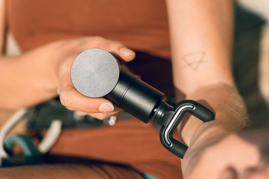 A close-up shot of a hand using a massage gun on an arm with a triangle tattoo visible.