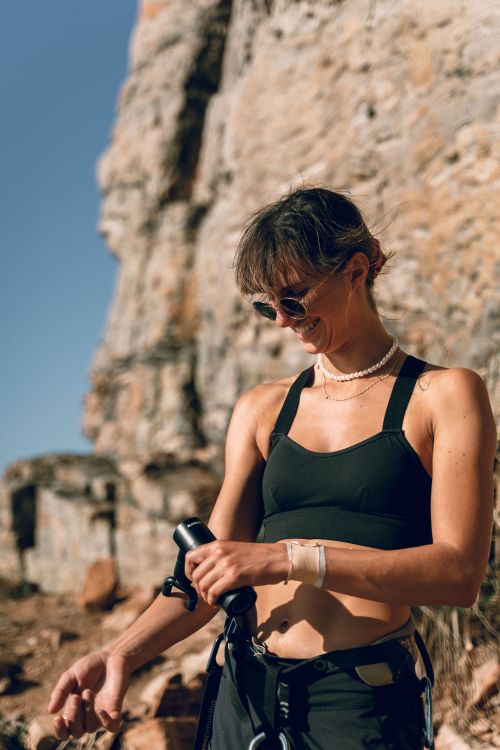 Free Outdoor scene of a woman using a massage gun against a rocky background, wearing activewear. Stock Photo