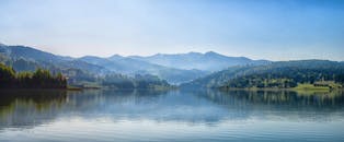 在晴朗的蓝天下，一个宁静的高山湖泊被薄雾笼罩的森林和远处的山峰环绕