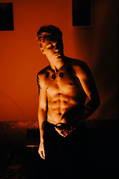 Free Moody portrait of a shirtless man with tattoos illuminated by warm lighting. Stock Photo