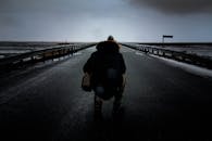 在阴沉昏暗的天空下，空旷潮湿的道路上一个人的剪影，透露出孤独