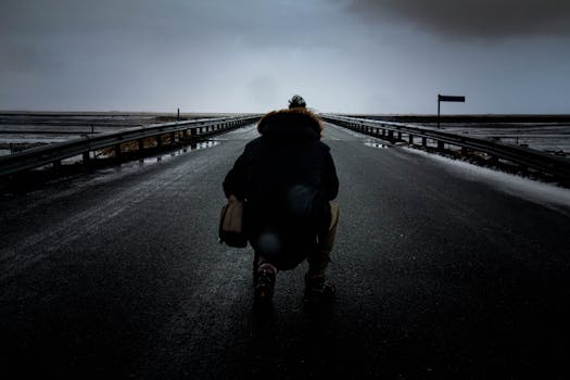 在阴沉昏暗的天空下，空旷潮湿的道路上一个人的剪影，透露出孤独