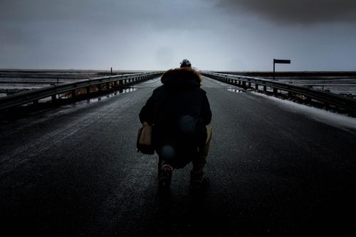 Free Silhouette of a person on an empty wet road under a dark, moody sky, suggesting solitude. Stock Photo