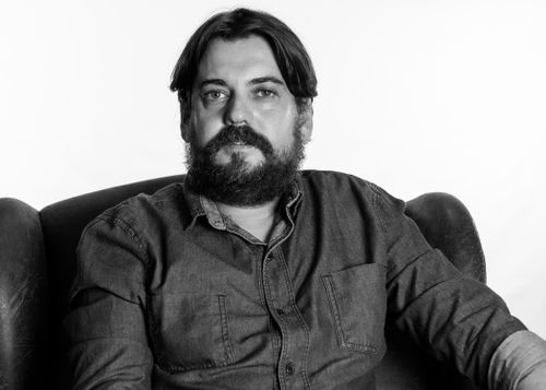 Free Black and white portrait of a bearded man sitting in a relaxed pose, showcasing facial hair and monochrome style. Stock Photo
