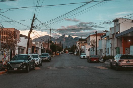An urban street scene in Monterrey, Mexico with cars parked and mountains in the background.