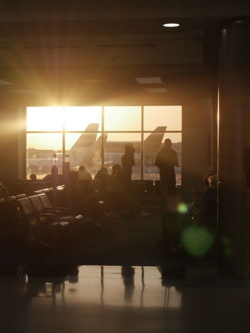 Free Passengers await flights at Orlando Airport with sunset in the background, creating silhouettes. Stock Photo
