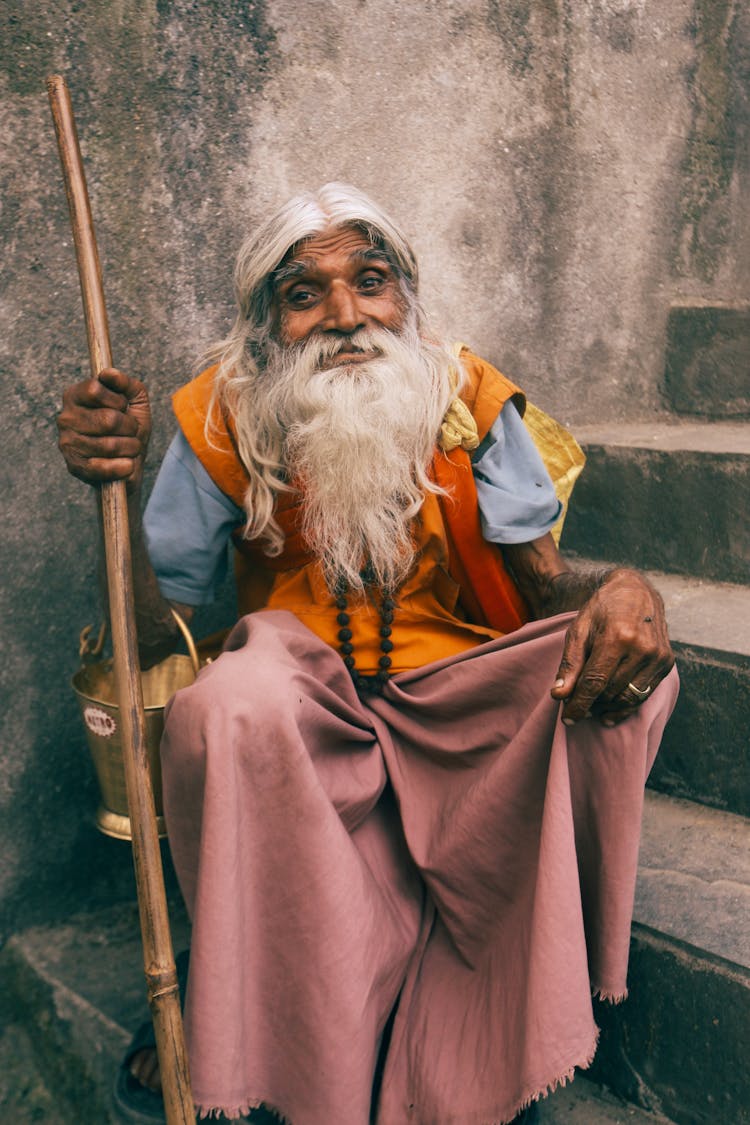 Old Indian Man With Stick In Hand Sitting On Stairs