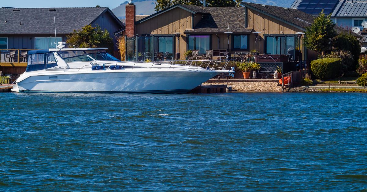 Elegant yacht docked by a waterfront home on a sunny day, showcasing luxury living.