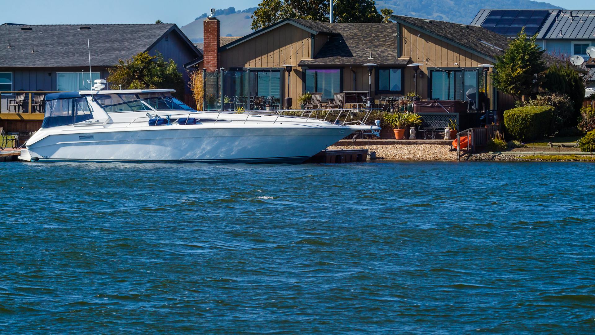 Elegant yacht docked by a waterfront home on a sunny day, showcasing luxury living.