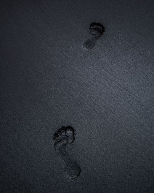 A high-angle view of two footprints on dark sand, capturing a serene nighttime beach atmosphere.