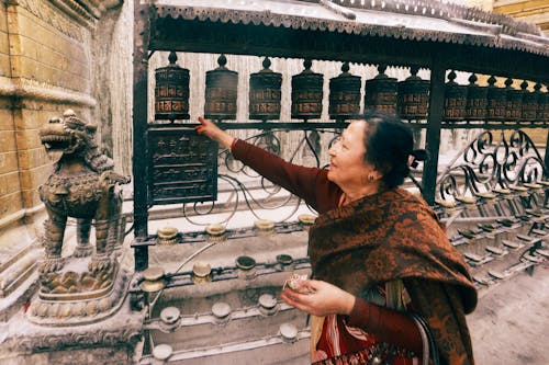 Senior Woman Rotating Prayer Wheels at Buddhist Temple