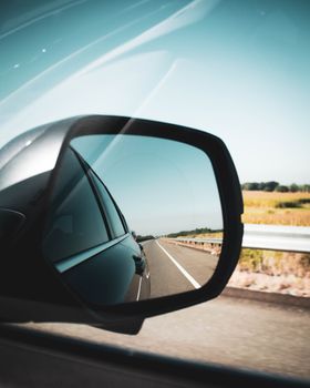 Close-up of car side mirror showing clear highway and fields under blue sky.