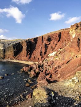 A breathtaking view of the iconic red cliffs at Red Beach, Santorini, Greece, under a clear blue sky.