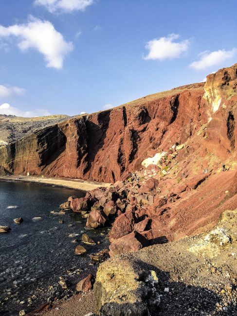 A breathtaking view of the iconic red cliffs at Red Beach, Santorini, Greece, under a clear blue sky.