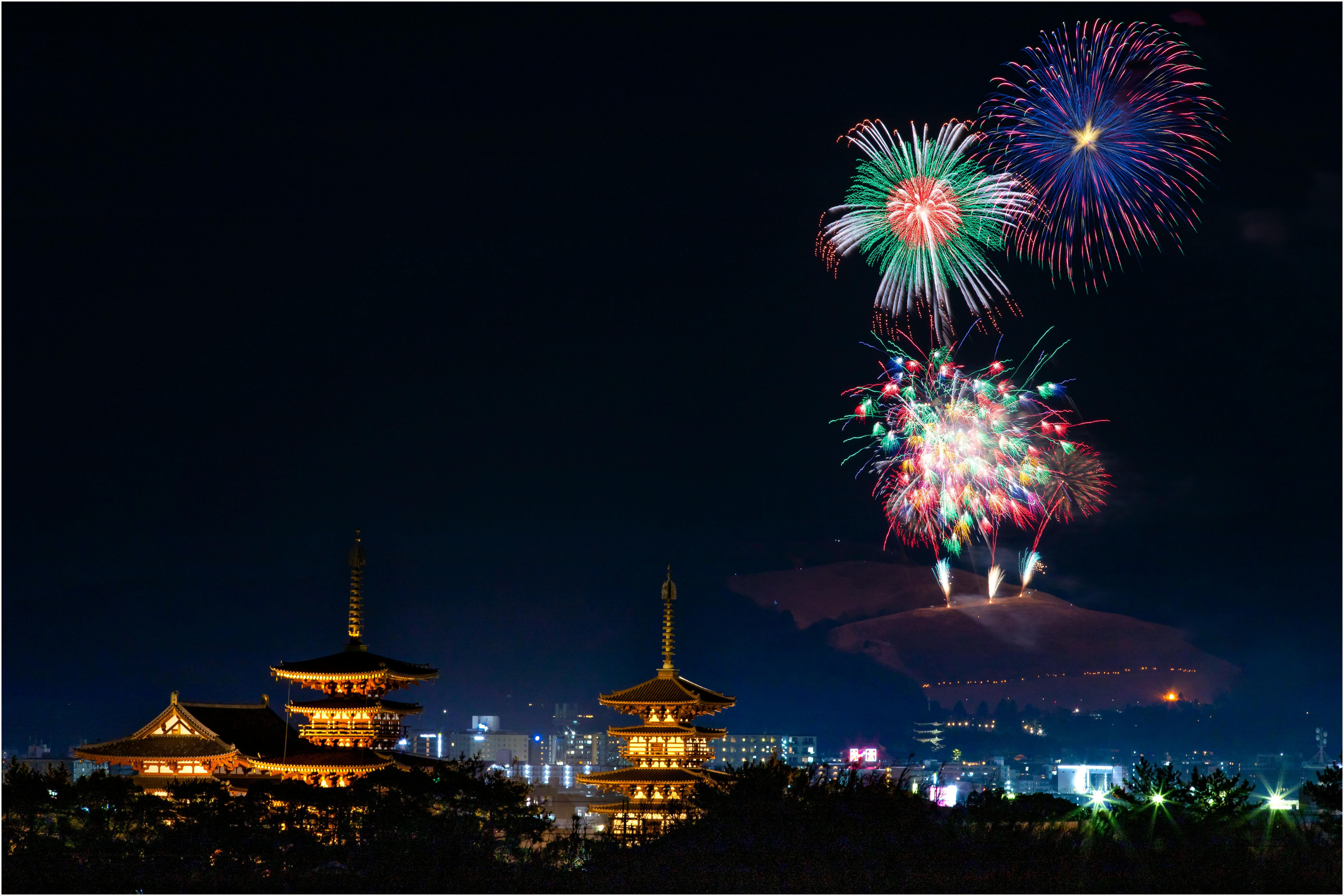 Vibrant fireworks light up the night sky above a beautifully illuminated pagoda and cityscape.