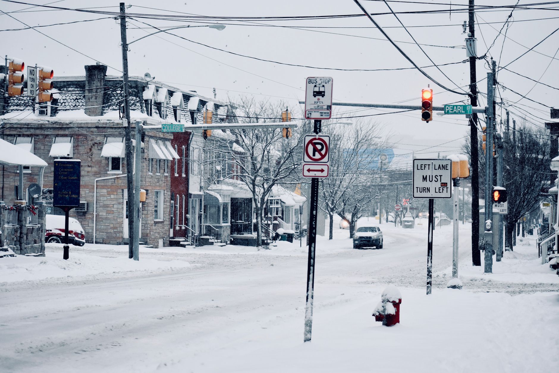 A winter street view in Lancaster, PA showcasing snowy roads, traffic signs, and parked vehicles.