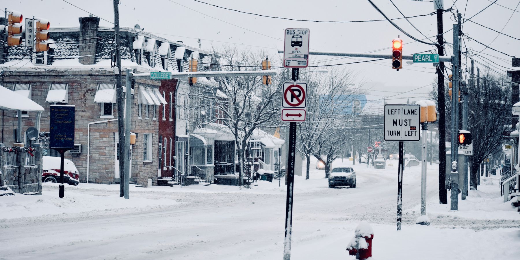 A winter street view in Lancaster, PA showcasing snowy roads, traffic signs, and parked vehicles.