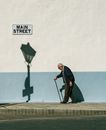 Man in Black Coat Holding Black Umbrella Walking on Sidewalk